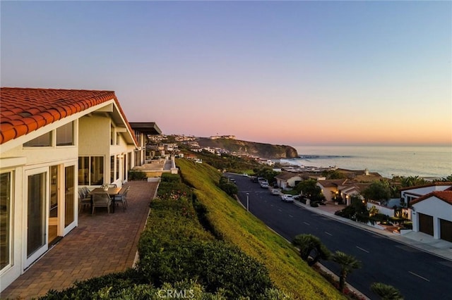 exterior space featuring a water view, stucco siding, a patio area, and a tiled roof