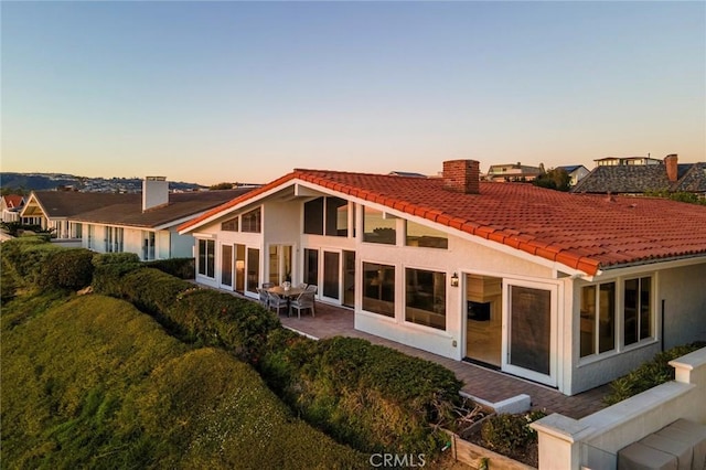 rear view of property featuring stucco siding, a tiled roof, a chimney, and a patio