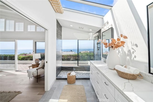 interior space with a skylight, double vanity, a water view, a sink, and wood finished floors