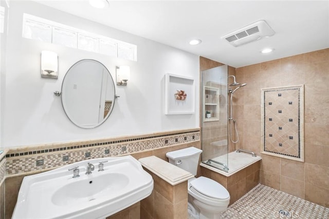 full bathroom with visible vents, wainscoting, toilet, a tile shower, and tile walls