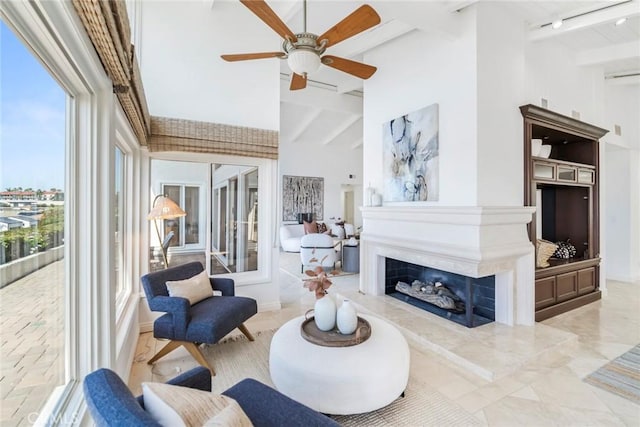 living room with a high ceiling, a fireplace, beam ceiling, and a ceiling fan