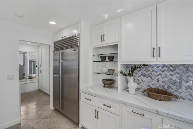 kitchen featuring light stone countertops, white cabinetry, baseboards, decorative backsplash, and stainless steel built in refrigerator