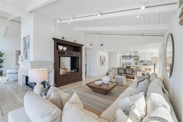 living room featuring a fireplace with raised hearth, vaulted ceiling with beams, visible vents, and track lighting