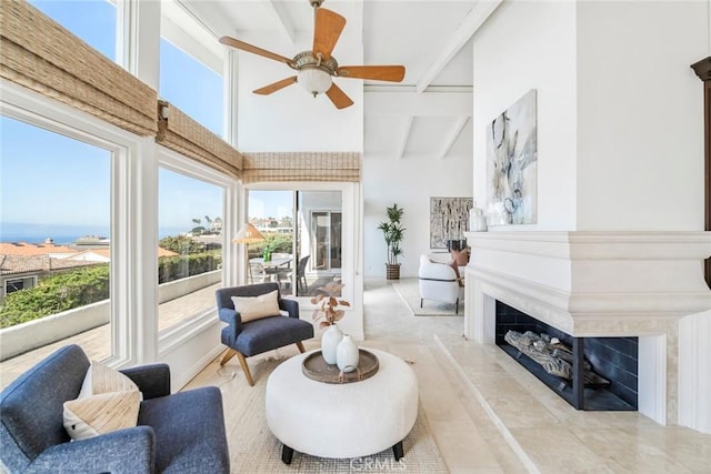 living area with a ceiling fan, a premium fireplace, a high ceiling, and beam ceiling