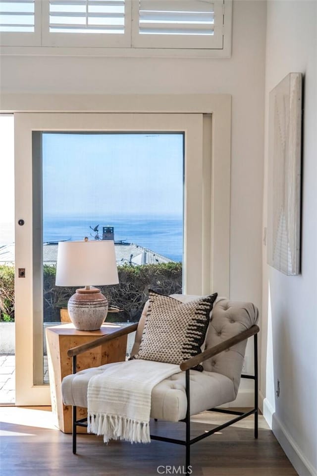 sitting room with a water view, a towering ceiling, baseboards, and dark wood-style flooring