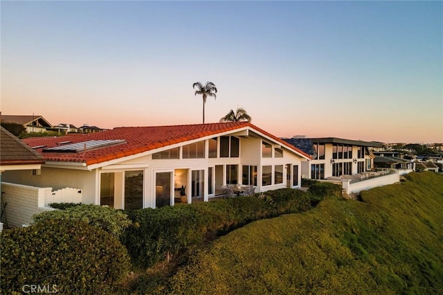 back of house at dusk with a tile roof and stucco siding