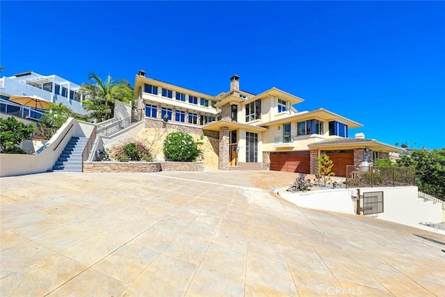 view of front of home featuring concrete driveway, stone siding, stairway, an attached garage, and stucco siding