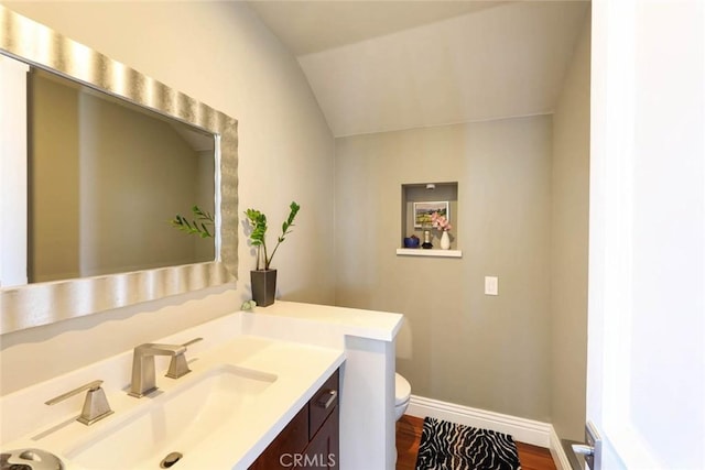 half bath featuring baseboards, toilet, wood finished floors, vaulted ceiling, and vanity