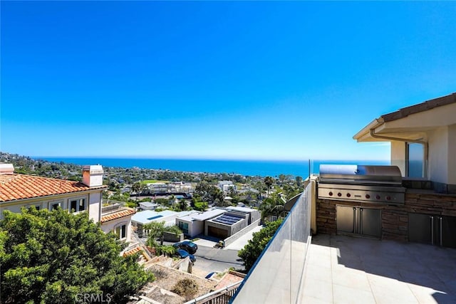 balcony with exterior kitchen, area for grilling, and a water view