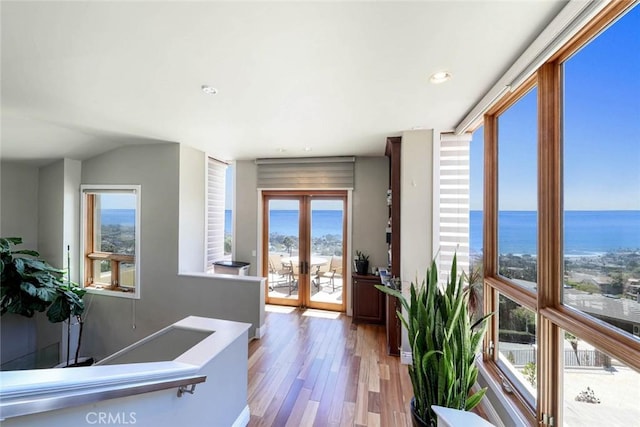 corridor featuring a water view, light wood-type flooring, recessed lighting, and french doors