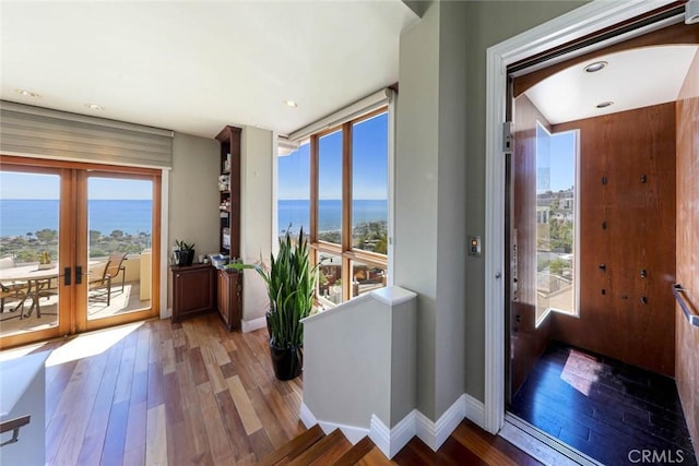 doorway to outside with a water view, baseboards, wood finished floors, and french doors