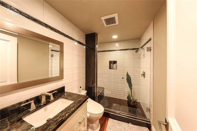 full bathroom featuring tile walls, visible vents, toilet, a shower stall, and vanity