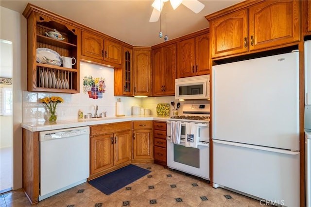 kitchen with a ceiling fan, a sink, white appliances, brown cabinetry, and glass insert cabinets