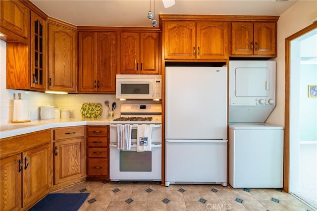 kitchen featuring stacked washer and clothes dryer, brown cabinets, white appliances, and glass insert cabinets