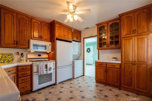 kitchen with white appliances, brown cabinetry, visible vents, and stacked washer / drying machine