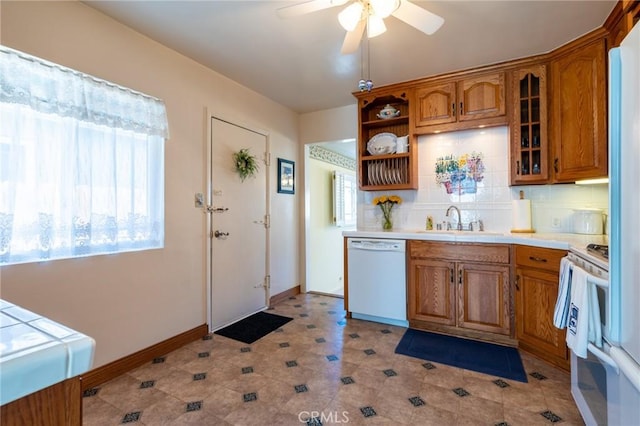 kitchen with tasteful backsplash, light countertops, brown cabinets, white appliances, and a sink