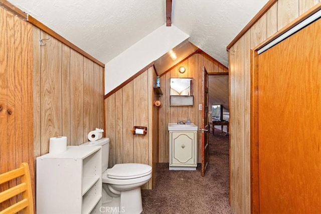 half bathroom featuring toilet, a sink, vaulted ceiling, wood walls, and a textured ceiling