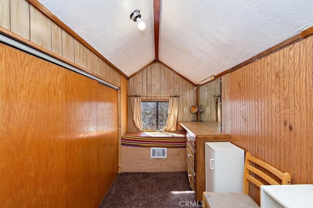 interior space featuring lofted ceiling, wood walls, a textured ceiling, and visible vents