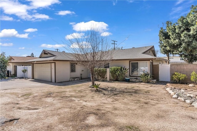 ranch-style house featuring driveway, fence, an attached garage, and stucco siding