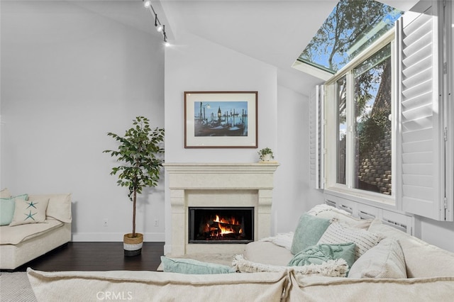 sitting room featuring lofted ceiling, wood finished floors, baseboards, a warm lit fireplace, and rail lighting