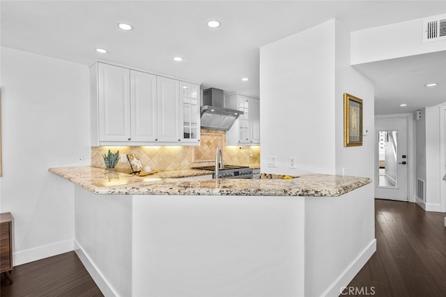 kitchen with visible vents, a peninsula, wall chimney range hood, and light stone countertops