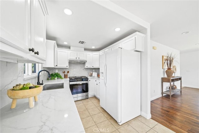 kitchen with white refrigerator with ice dispenser, gas range, light stone countertops, under cabinet range hood, and a sink