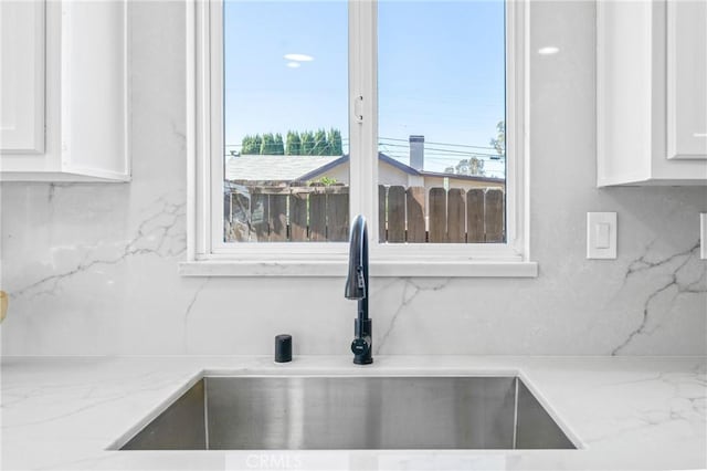 details featuring light stone counters, decorative backsplash, white cabinets, and a sink