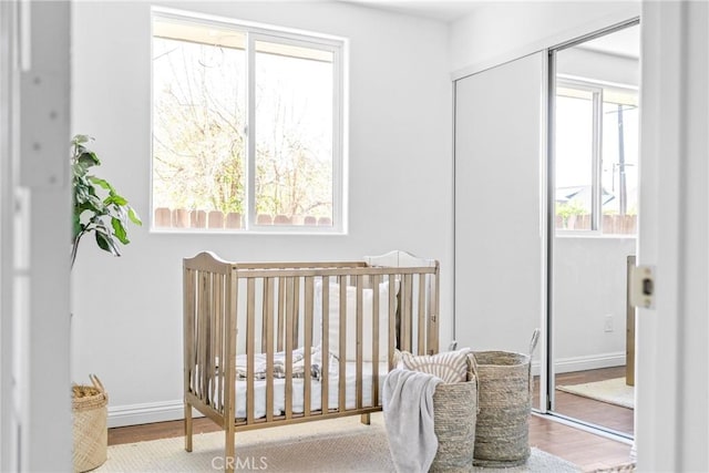 bedroom featuring a crib, a closet, baseboards, and wood finished floors