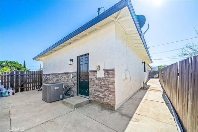 view of home's exterior with a fenced backyard, cooling unit, stone siding, stucco siding, and a patio area