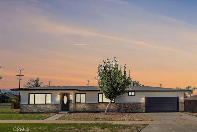 view of front of property featuring concrete driveway, stone siding, an attached garage, and stucco siding