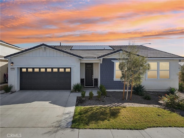 view of front of house with a garage, roof mounted solar panels, and driveway