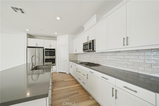 kitchen featuring dark countertops, visible vents, appliances with stainless steel finishes, white cabinetry, and a sink