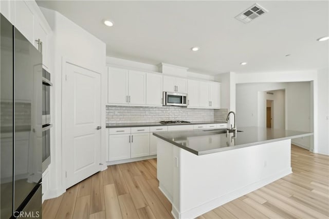 kitchen featuring visible vents, white cabinets, an island with sink, stainless steel appliances, and a sink