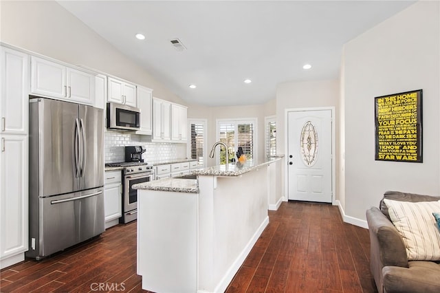 kitchen with light stone counters, visible vents, white cabinetry, appliances with stainless steel finishes, and a center island with sink