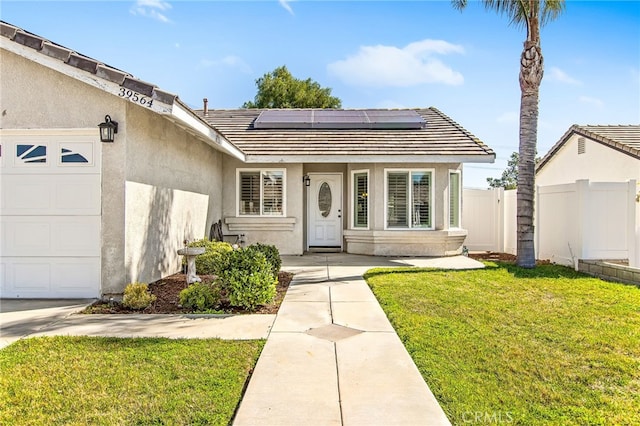 entrance to property with a yard, stucco siding, solar panels, an attached garage, and fence