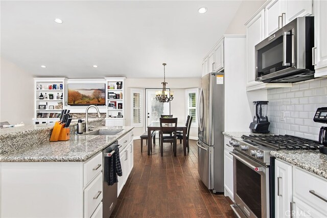 kitchen featuring appliances with stainless steel finishes, light stone counters, hanging light fixtures, white cabinetry, and a sink