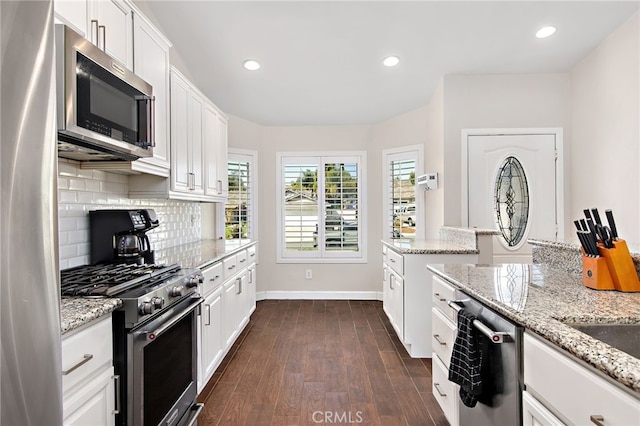 kitchen with stainless steel appliances, dark wood-style flooring, white cabinetry, light stone countertops, and tasteful backsplash