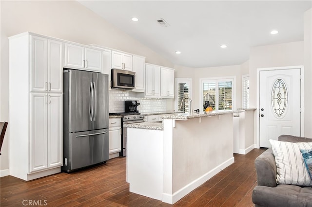 kitchen with a center island with sink, dark wood finished floors, appliances with stainless steel finishes, vaulted ceiling, and white cabinetry