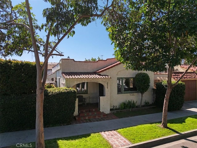 mediterranean / spanish home with a fenced front yard, a tiled roof, and stucco siding