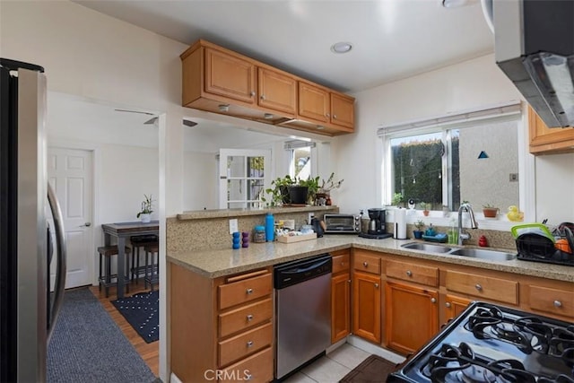 kitchen featuring brown cabinetry, appliances with stainless steel finishes, a peninsula, light stone countertops, and a sink