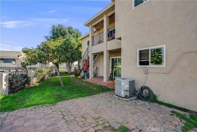 exterior space featuring a lawn, fence, cooling unit, a patio area, and stucco siding