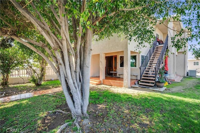 exterior space featuring stucco siding, a lawn, stairway, central AC unit, and fence