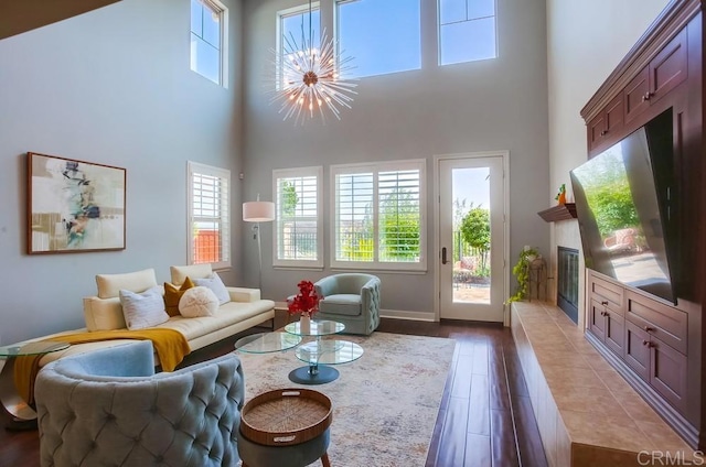 living room with dark wood finished floors, a glass covered fireplace, baseboards, and a towering ceiling