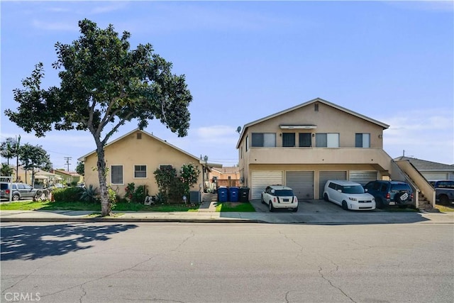 view of front facade with a garage, driveway, central AC unit, and stucco siding