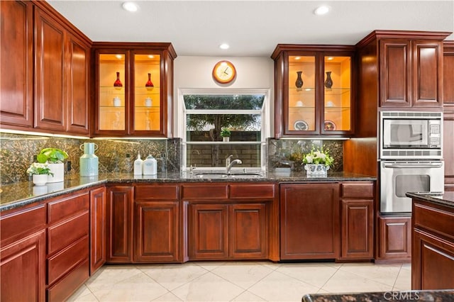 kitchen with backsplash, appliances with stainless steel finishes, a sink, dark stone countertops, and dark brown cabinets