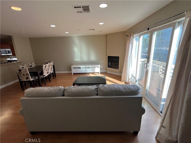 living area with recessed lighting, visible vents, wood finished floors, and a glass covered fireplace