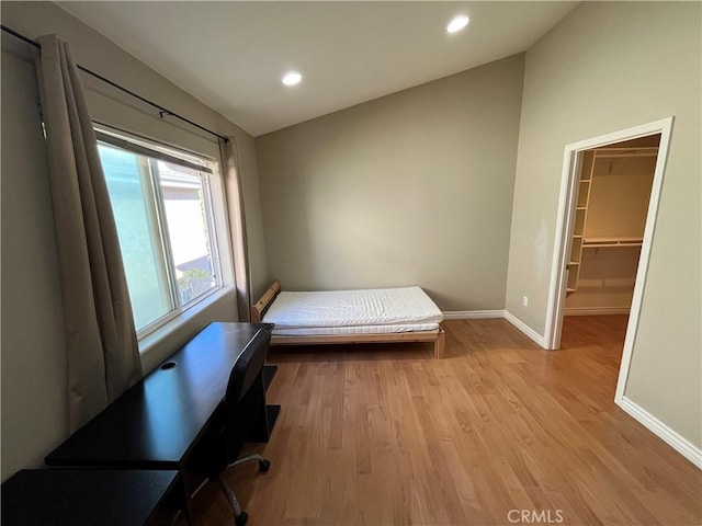 bedroom with recessed lighting, a walk in closet, light wood-style flooring, and baseboards