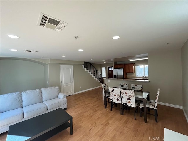 living area featuring stairway, light wood-type flooring, visible vents, and baseboards