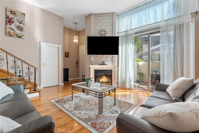 living room featuring a glass covered fireplace, stairway, wood finished floors, and baseboards