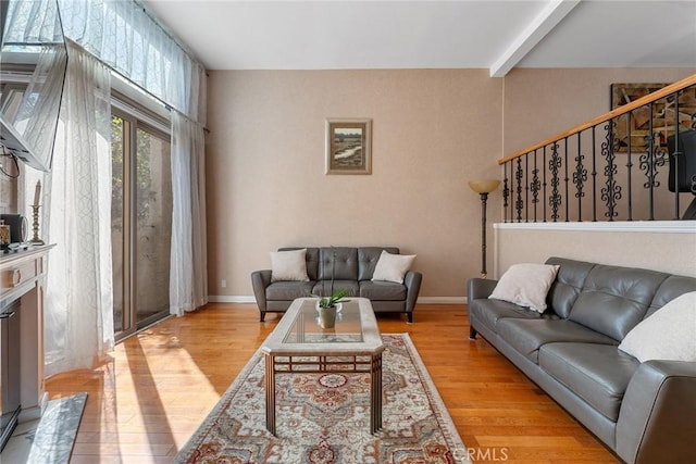 living room with light wood-type flooring, beamed ceiling, baseboards, and stairs